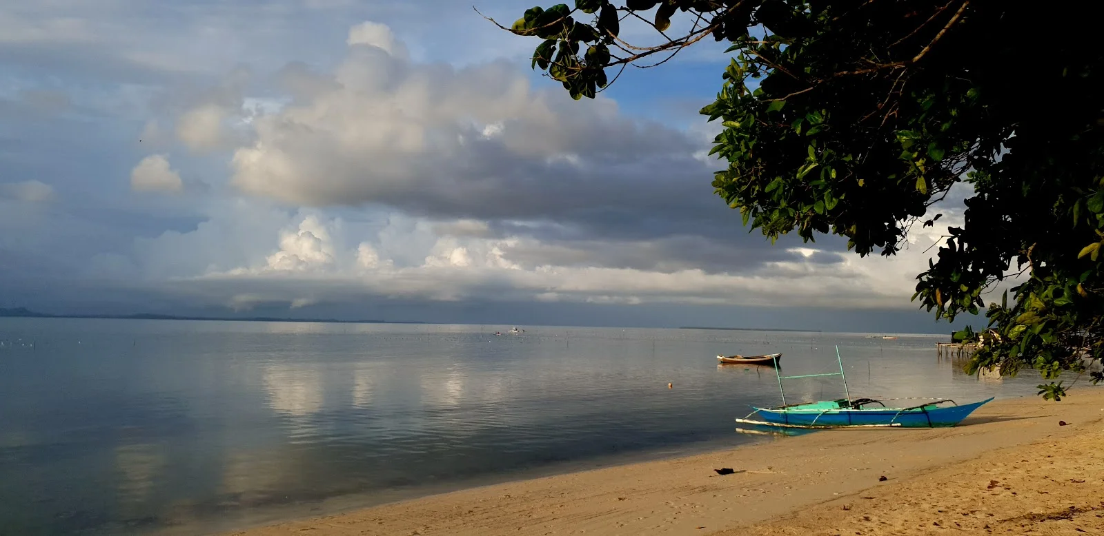 Bangka bleue amarrée sur une plage calme de Bancalan sous un ciel nuageux