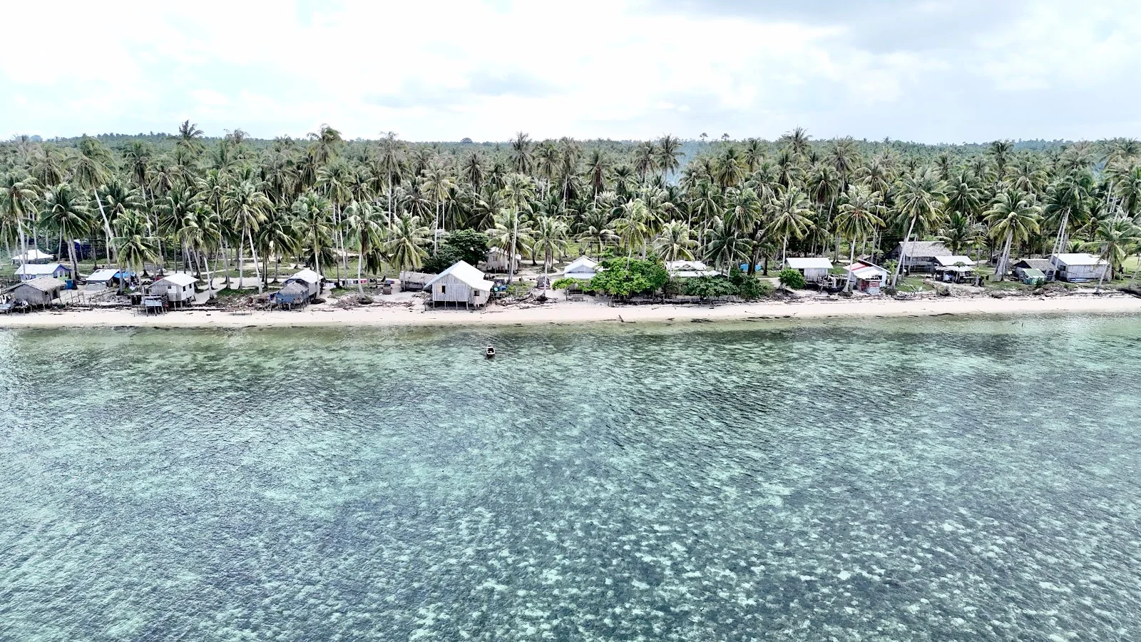Village côtier de Bancalan vu du ciel — maisons en bois sous les cocotiers, récif affleurant