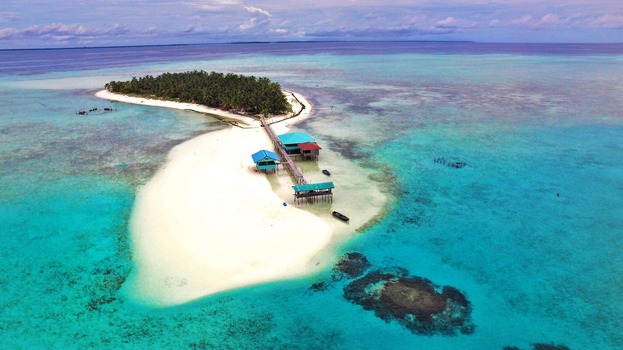 Onok Island vue du ciel — îlot boisé, langue de sable blanc et kubos sur pilotis reliés par un ponton