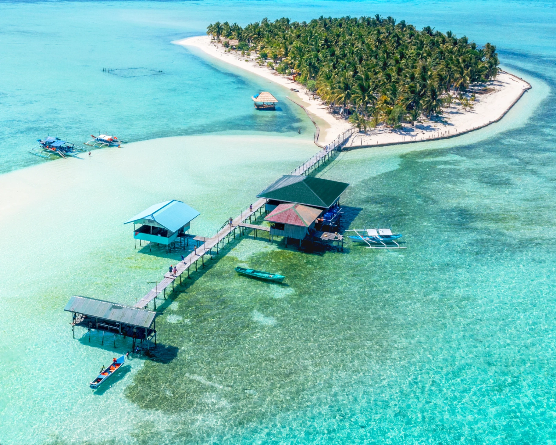 Vue aérienne signature d'Onok Island — banc de sable, pontons en bois et kubos sur pilotis dans un lagon translucide