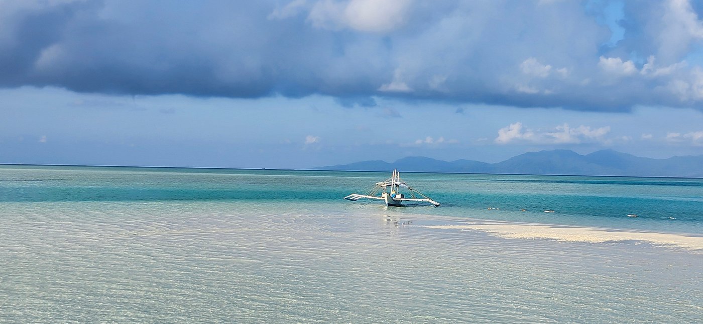 Bangka isolé sur un banc de sable submergé au large d'Onok, ciel voilé et montagnes à l'horizon