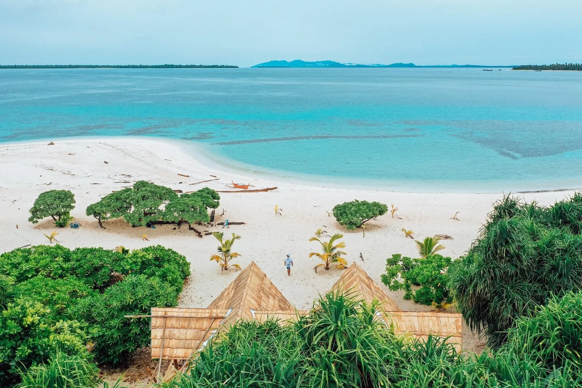 Petits abris en feuilles de palme sur la plage de Patawan, lagon calme en arrière-plan